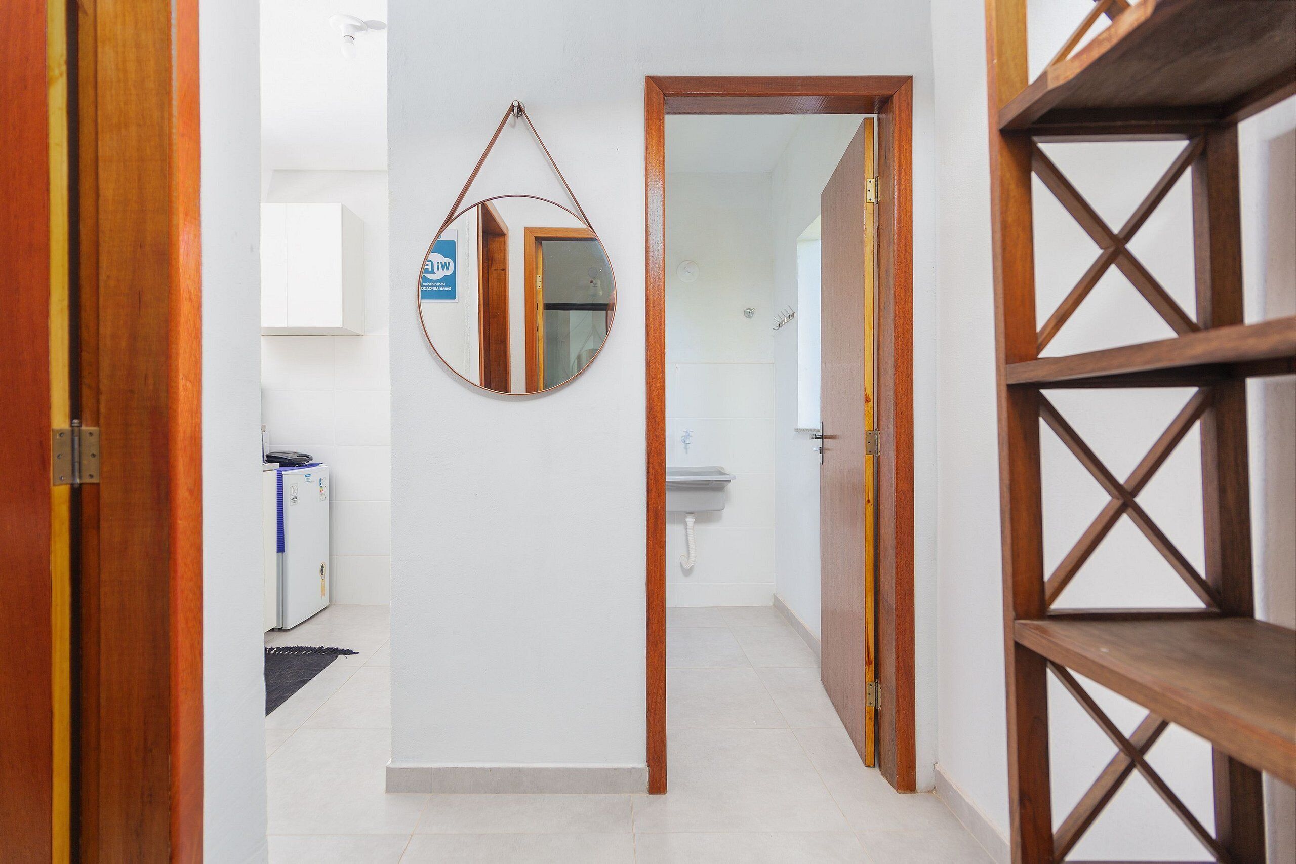 A hallway with a wooden door, a mirror, a white wall, and a white tiled floor.