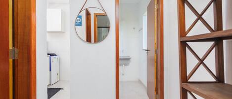 A hallway with a wooden door, a mirror, a white wall, and a white tiled floor.