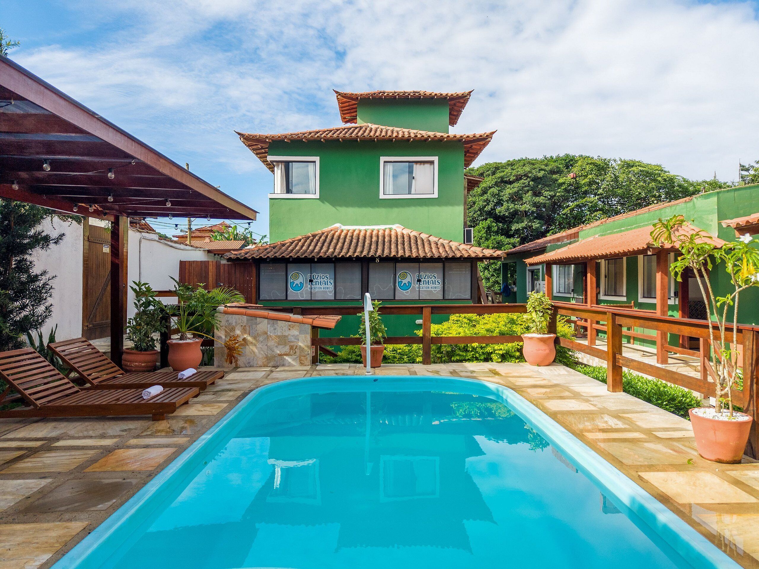 A poolside area with a green building, a wooden deck, and lounge chairs.