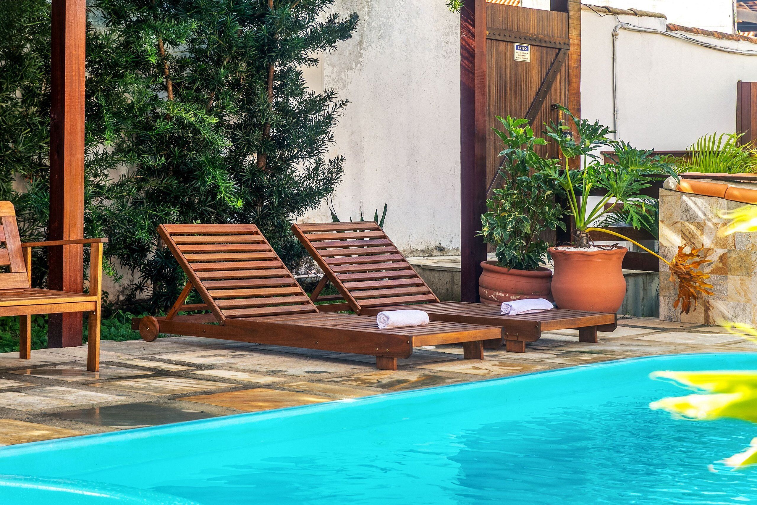 A poolside area with lounge chairs, a wooden table, and potted plants.