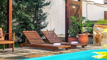A poolside area with lounge chairs, a wooden table, and potted plants.