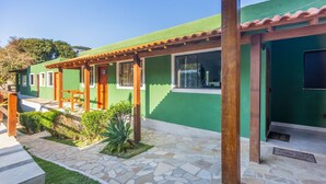 Un edificio verde con un patio cubierto, piso de piedra y un pequeño jardín.