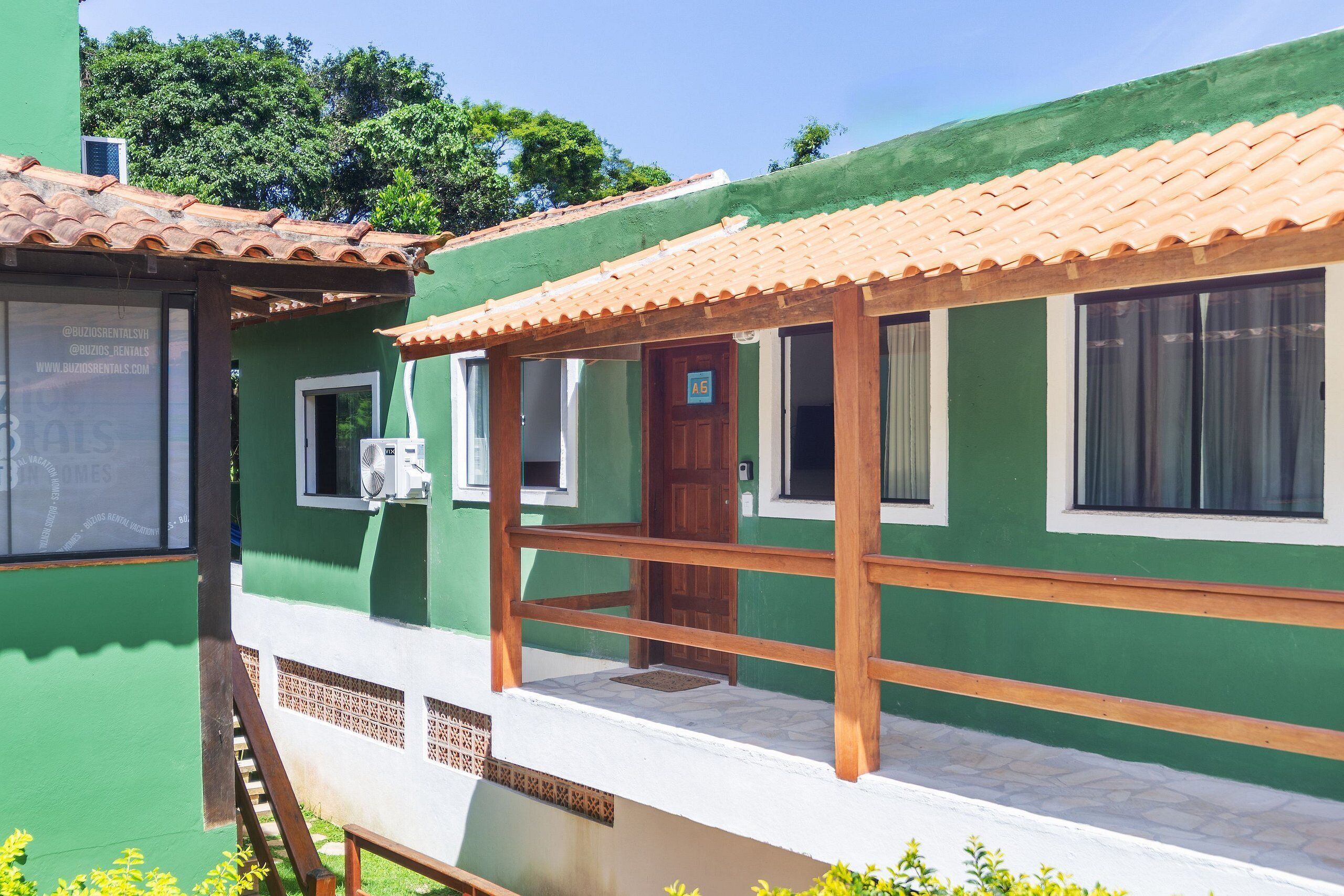 Um edifício verde com telhado ladrilhado, varanda de madeira e uma porta identificada como 'A6'.
