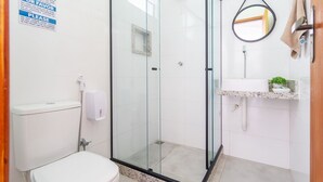 Un baño con cabina de ducha de vidrio, inodoro, lavabo con espejo y perchero para toallas.