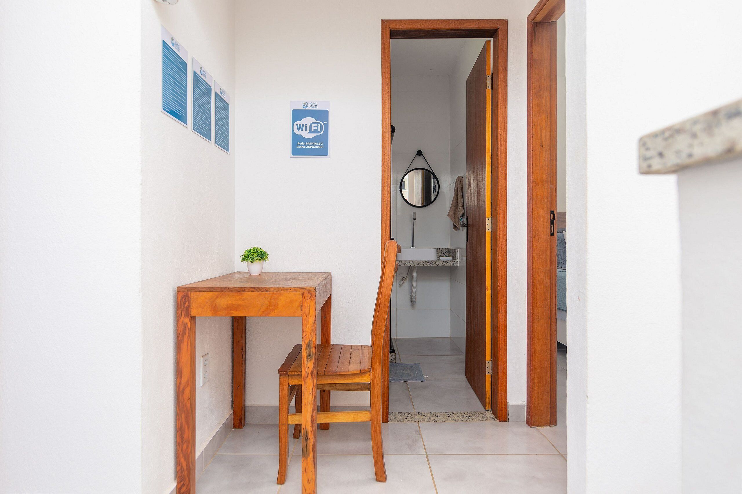 A small room with a wooden table and chair, a potted plant, a Wi-Fi sign, and a mirror on the wall.