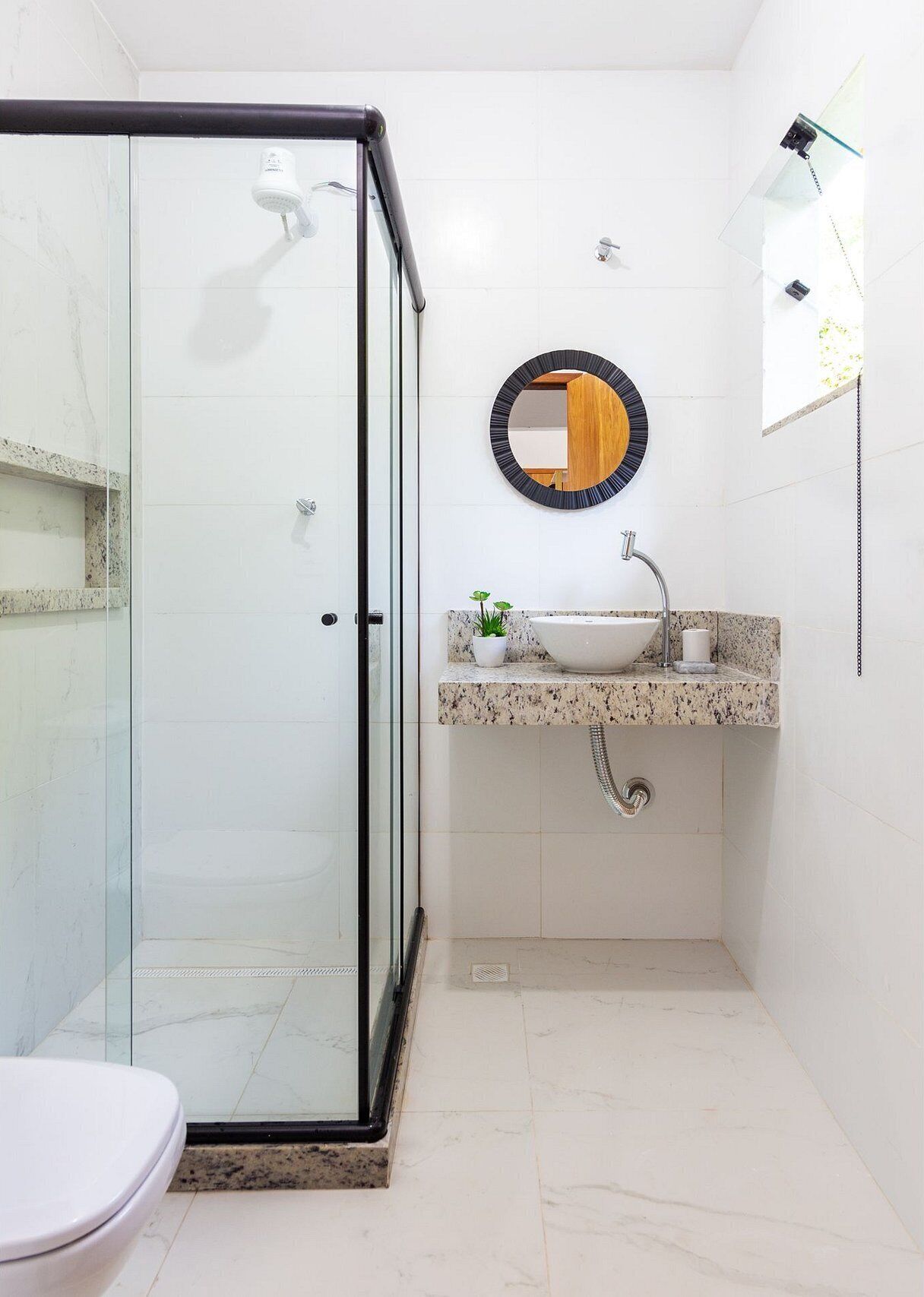 Un bagno con box doccia in vetro, lavandino con piano in marmo e specchio rotondo con cornice in legno.