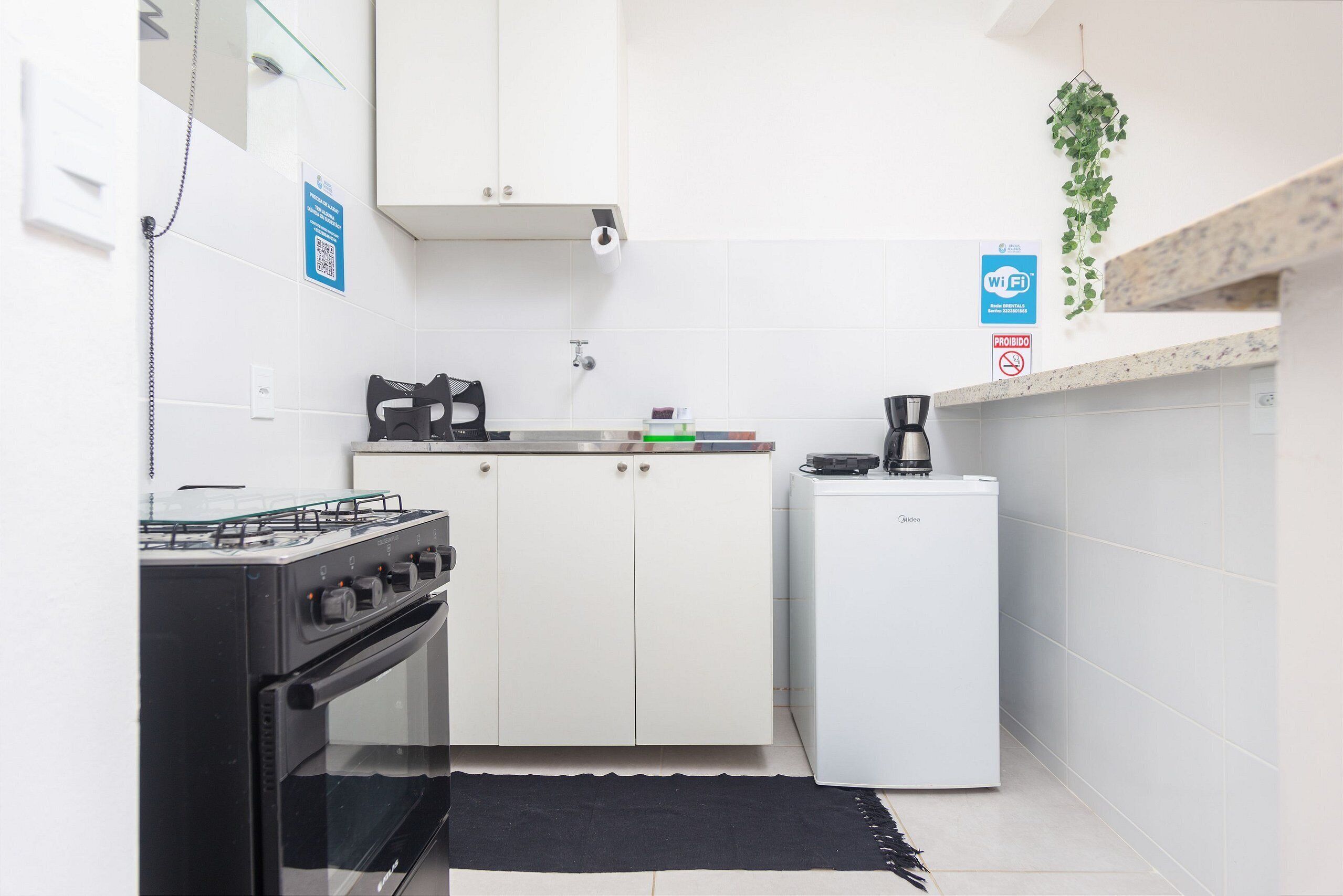 A compact kitchen with a gas stove, oven, white cabinets, a small refrigerator, and a coffee maker.