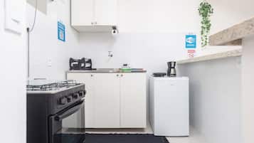A compact kitchen with a gas stove, oven, white cabinets, a small refrigerator, and a coffee maker.
