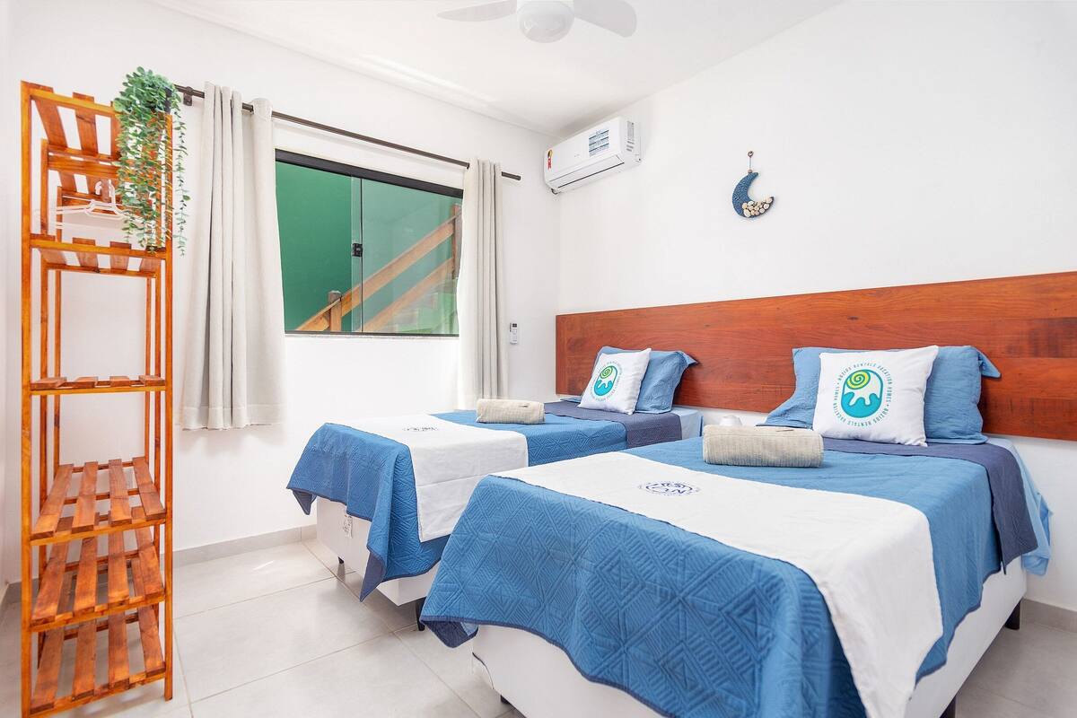 A hotel room with two beds, a wooden headboard, a plant, and a window with curtains.