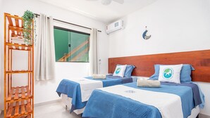 Habitación de hotel con dos camas, cabecera de madera, una planta y una ventana con cortinas.