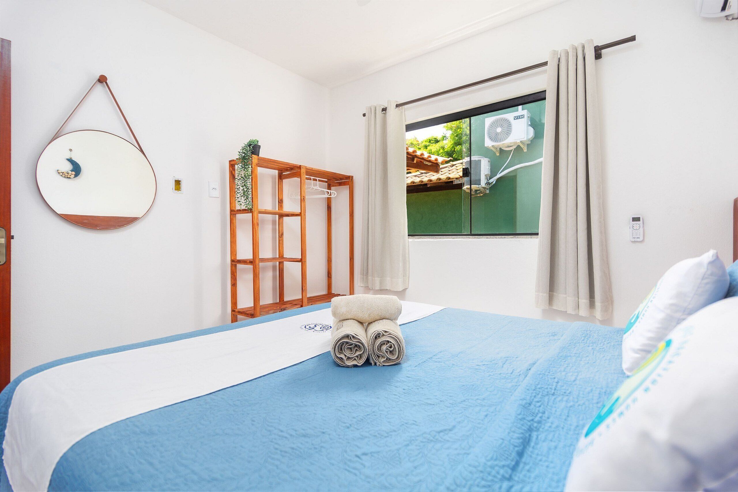 A bedroom with a bed, a window with curtains, a wall-mounted air conditioner, and a wooden shelf.