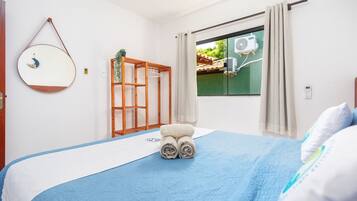 A bedroom with a bed, a window with curtains, a wall-mounted air conditioner, and a wooden shelf.
