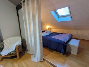 Une chambre mansardée accueillante, avec un puits de lumière, un lit, une chaise et une petite table de chevet.