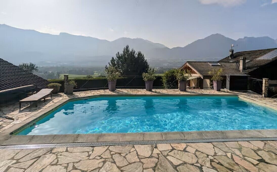 A swimming pool with stone tiles, potted plants, and a view of mountains in the background.