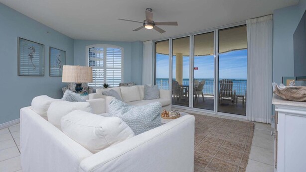 A spacious living room with a white sofa, a lamp, and a view of the ocean through large sliding glass doors. - Beach Colony East 3B (Pensacola)