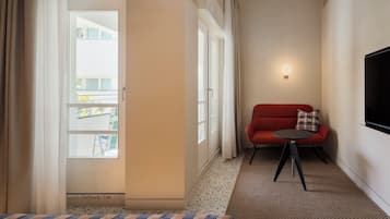 Une chambre d’hôtel avec un lit, un canapé rouge, une petite table, un téléviseur fixé au mur et une fenêtre avec des rideaux.