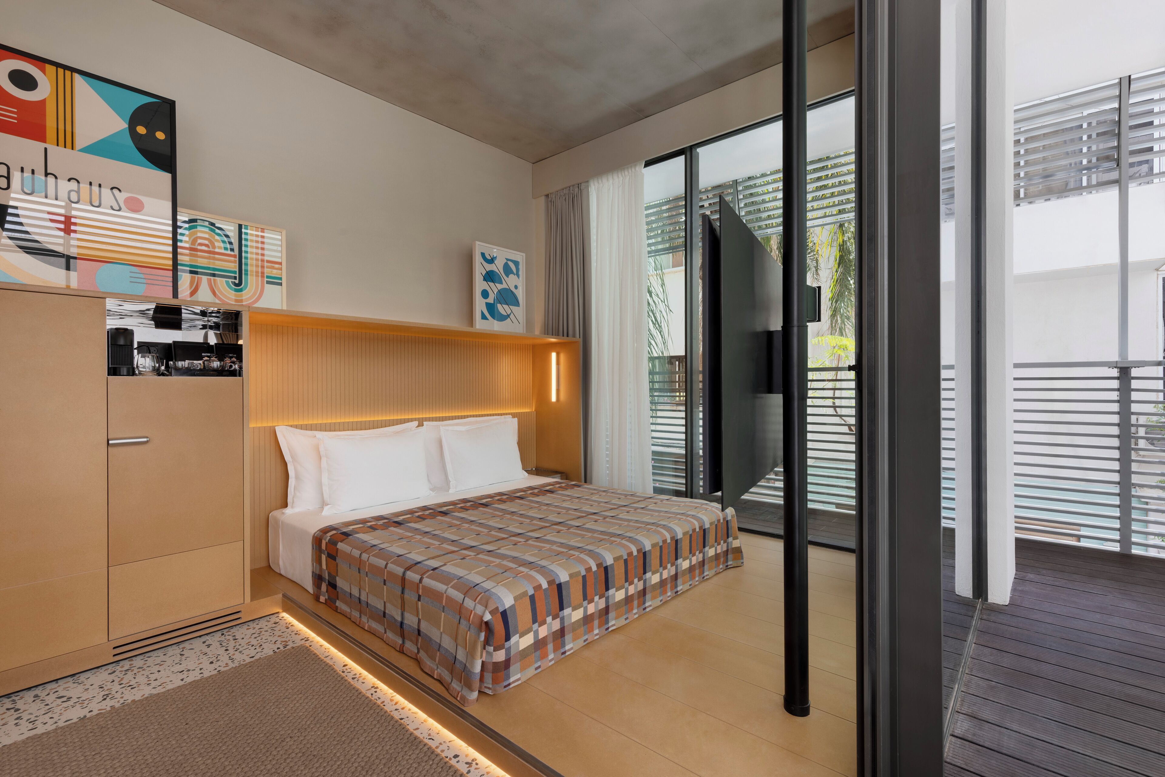 A modern hotel room with a bed, a wardrobe, a flat-screen TV, and a balcony with a view.