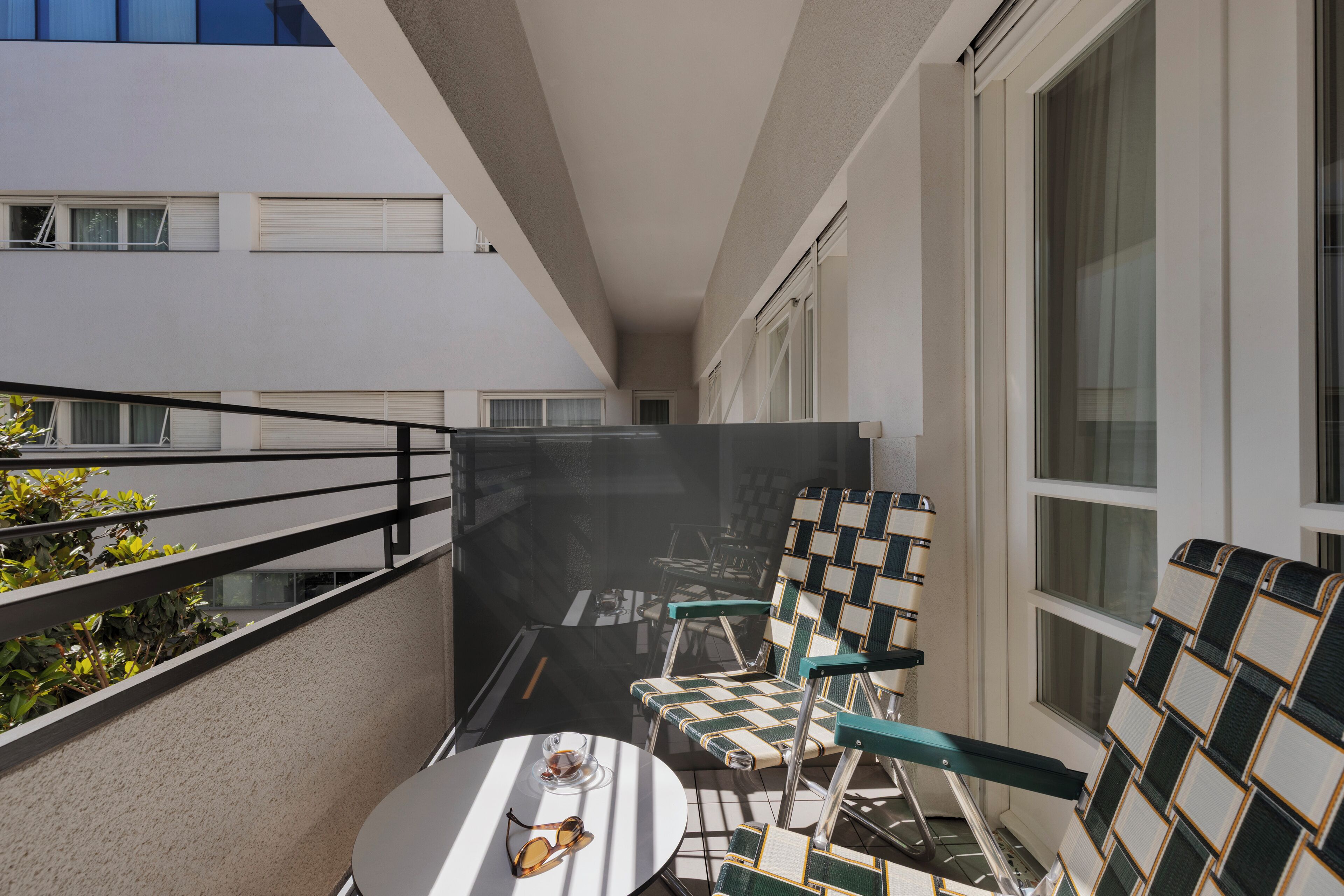 A balcony with a table and chairs, a glass railing, and a view of adjacent buildings.