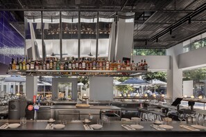 A bar area with a variety of liquor bottles, a seating area with tables and chairs, and a view of the outdoor seating area through large windows. - Dizengoff 99 by Isrotel Design (Tel Aviv)