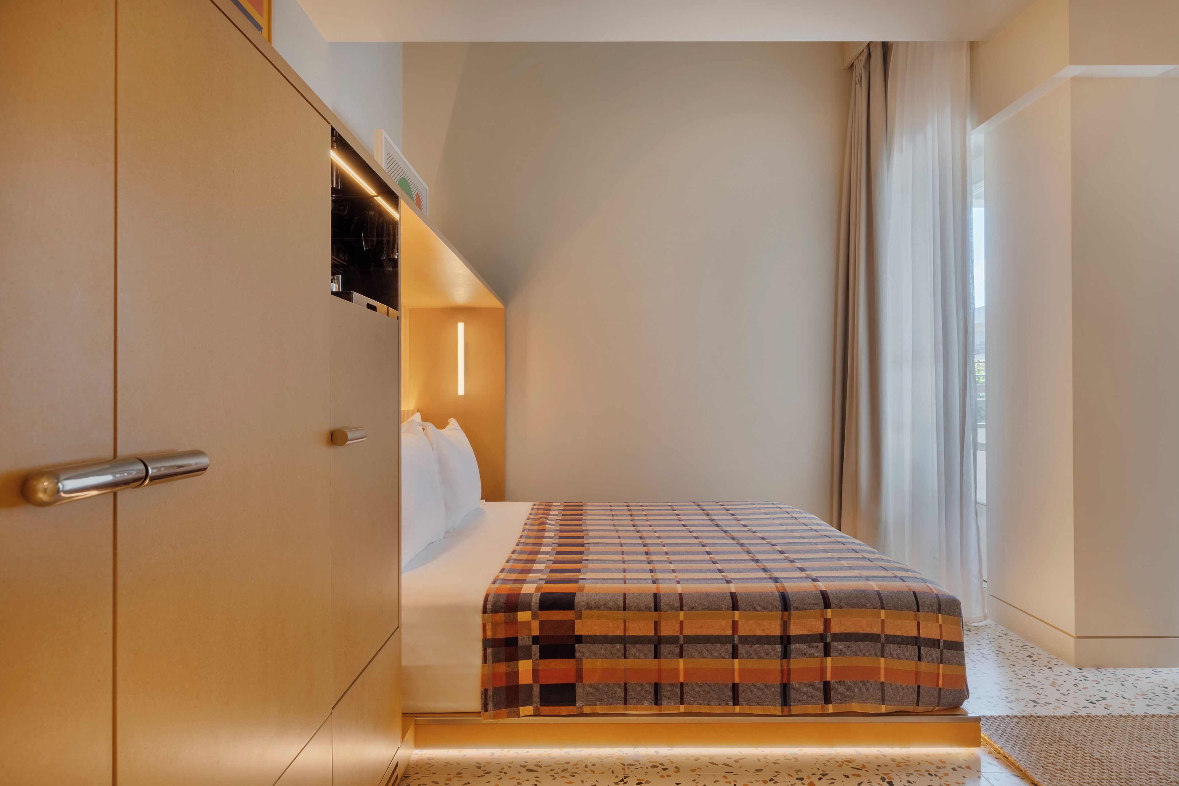 Quarto de hotel com cama, guarda-roupa, televisão na parede e janela com cortinas.