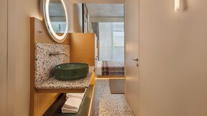 Une salle de bain avec un lavabo rond, un miroir avec éclairage intégré, un porte-serviettes et une vue sur un balcon.