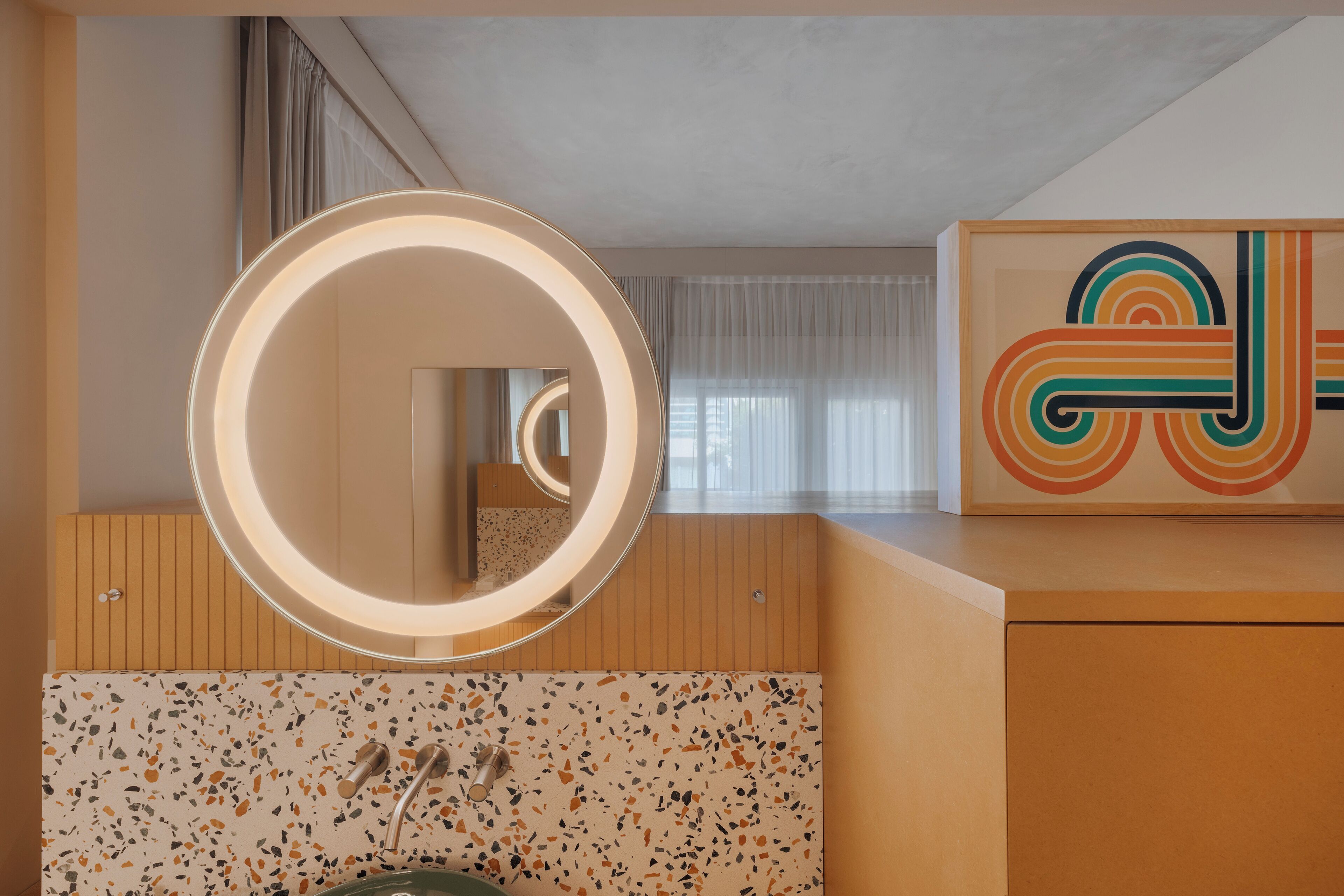Un baño moderno con un espejo redondo, salpicadero de baldosas con motas y tocador de madera.