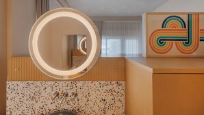Une salle de bain moderne avec un miroir rond, un pare-feu en carreaux à motifs et un meuble-lavabo en bois.