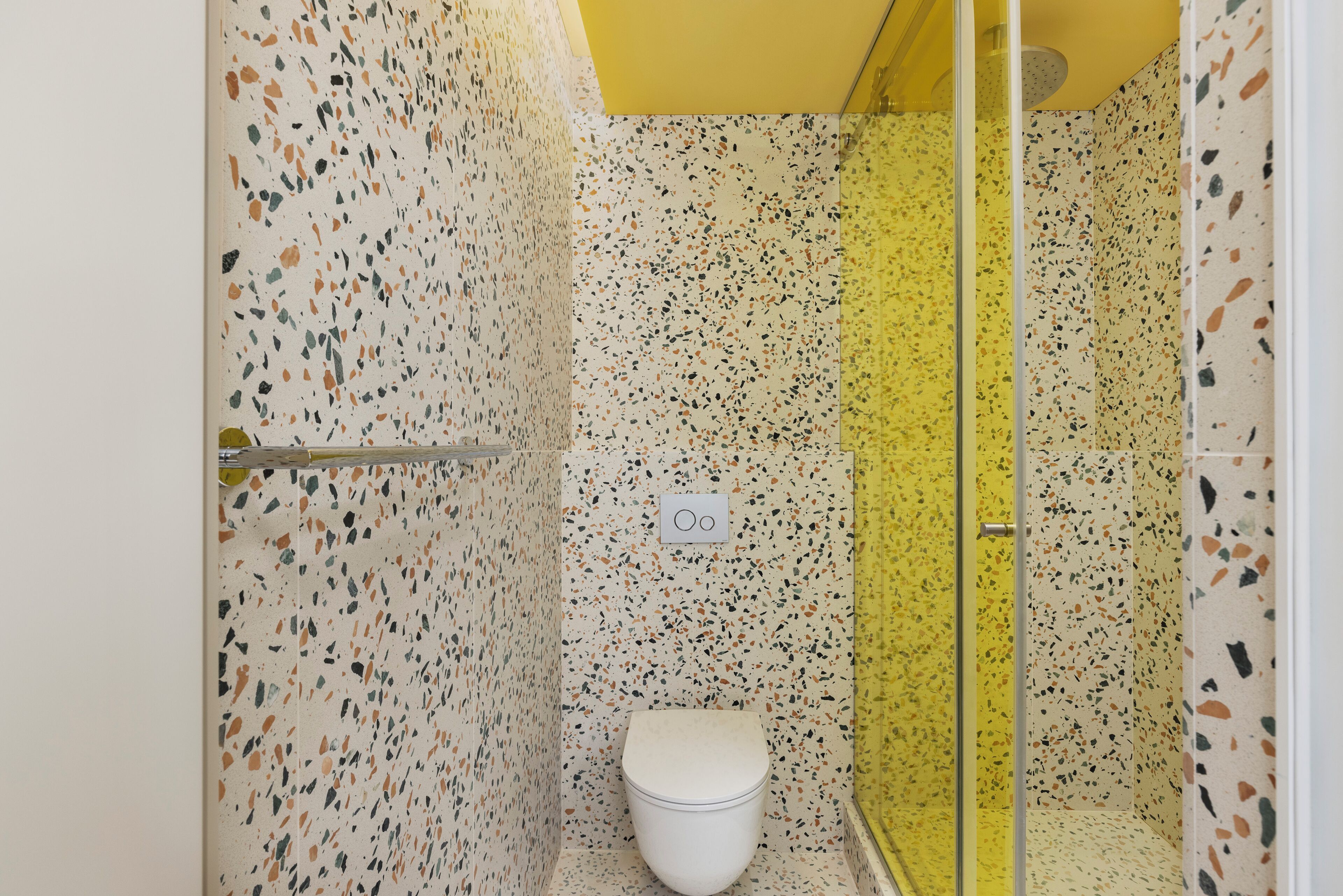 Un baño con inodoro blanco, ducha con puerta de cristal y pared con diseño de baldosas salpicadas.