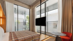 A modern hotel room with a bed, a TV, a small table, and a red chair.
