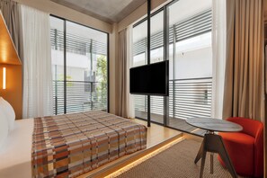 A modern hotel room with a bed, a TV, a small table, and a red chair. - Dizengoff 99 by Isrotel Design (Tel Aviv)