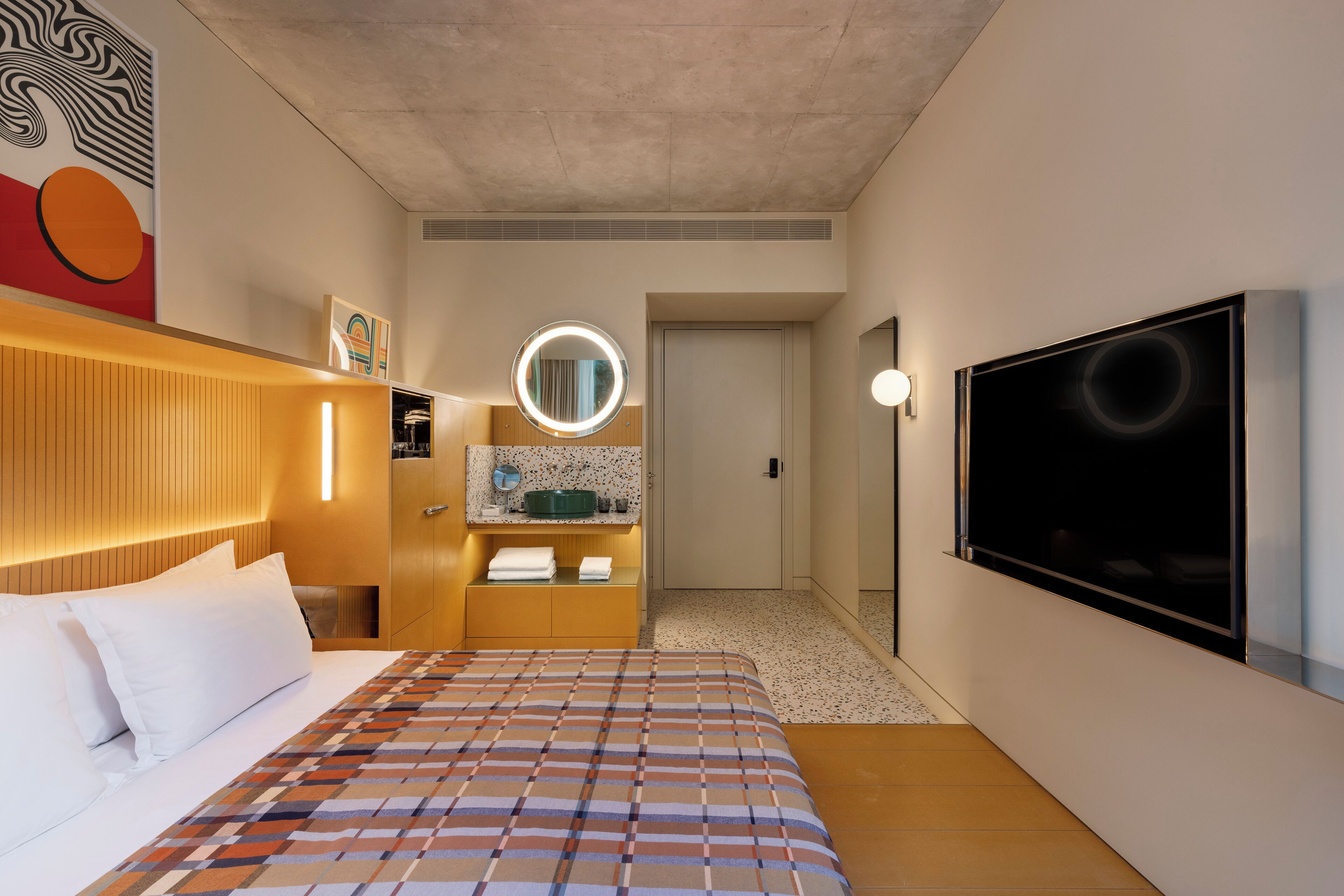 Een hotelkamer met een bed, een televisie, een badkamer met een spiegel en een deur die naar een andere kamer leidt.