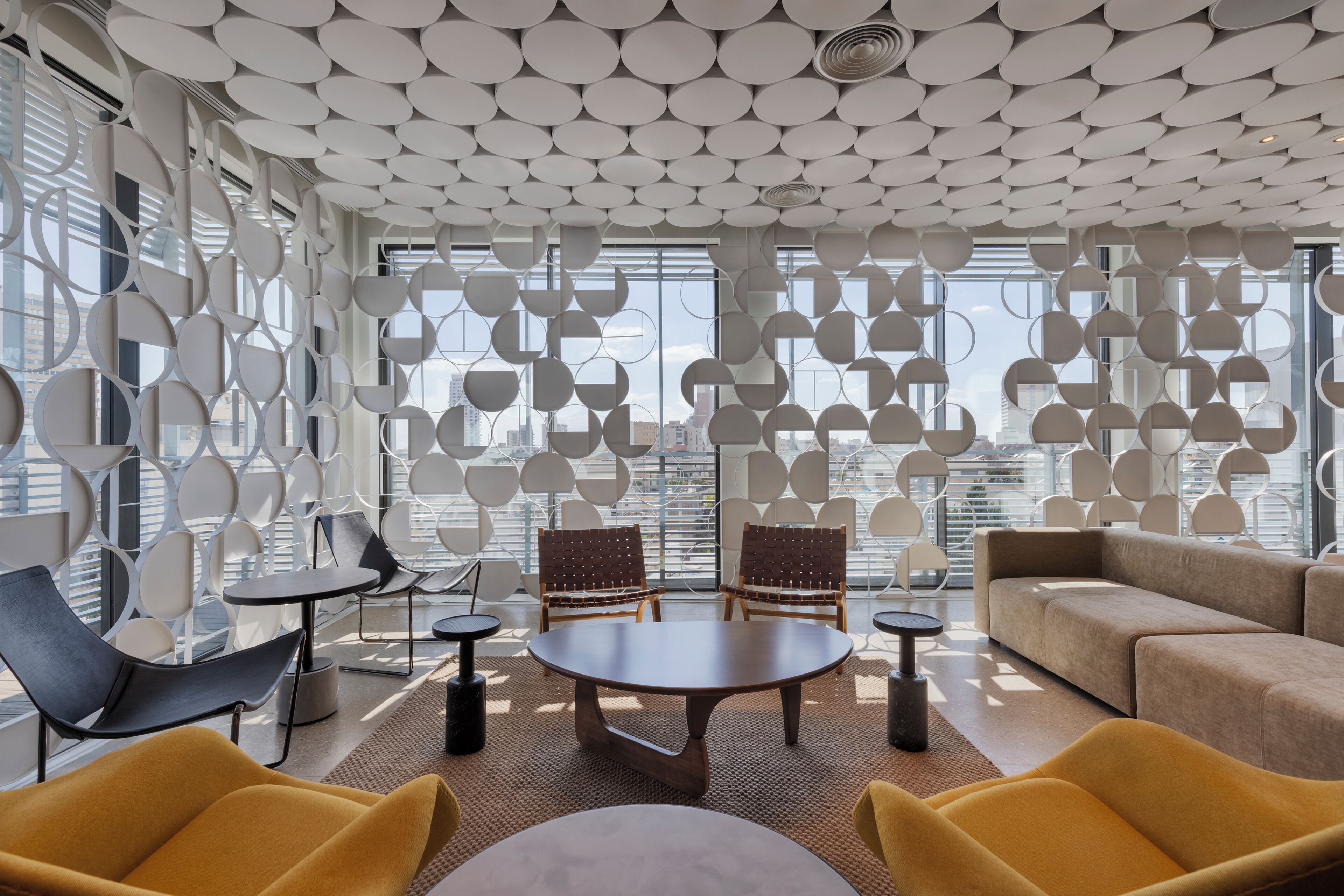 Un interior moderno con un diseño geométrico en el techo, ventanas amplias y muebles contemporáneos.