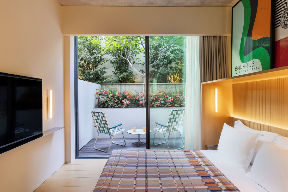 Una camera d'albergo con un letto, una televisione, un balcone con sedie e vista sul verde.