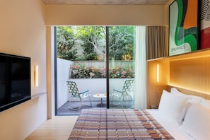 A hotel room with a bed, a TV, a balcony with chairs, and a view of greenery. - Dizengoff 99 by Isrotel Design (Tel Aviv)