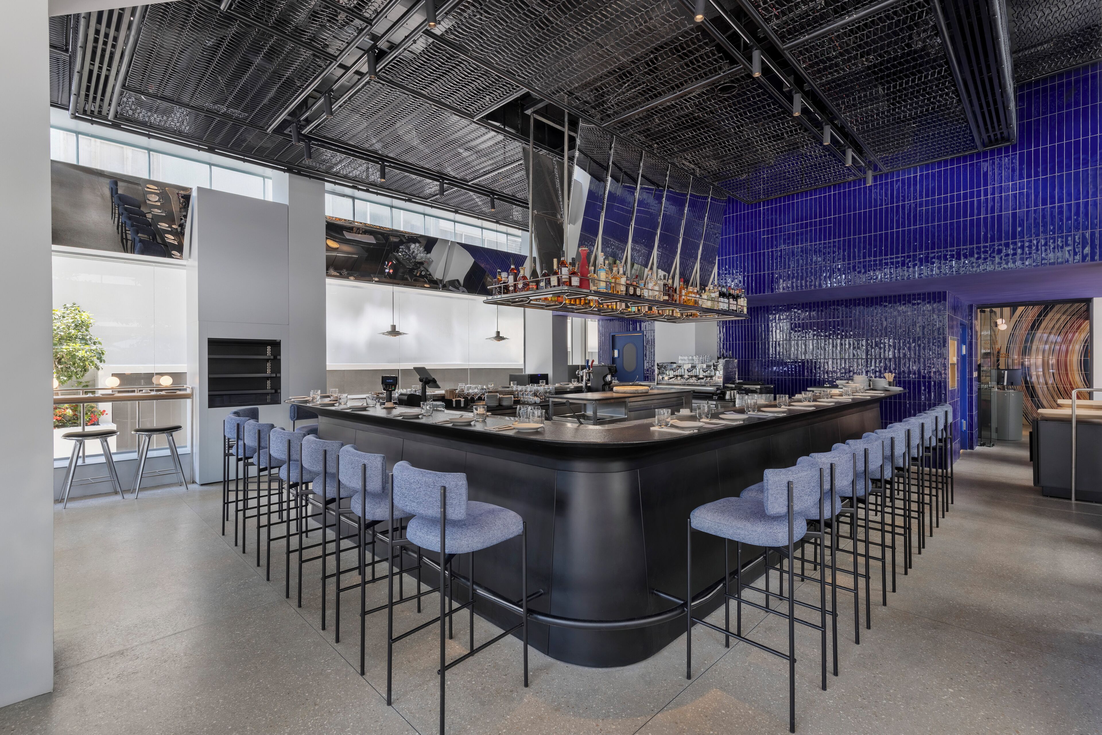 A modern bar area with a curved counter, bar stools, and a high ceiling with a metal grid design.