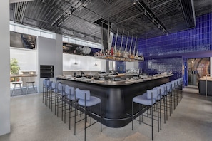 A modern bar area with a curved counter, bar stools, and a high ceiling with a metal grid design. - Dizengoff 99 by Isrotel Design (Tel Aviv)