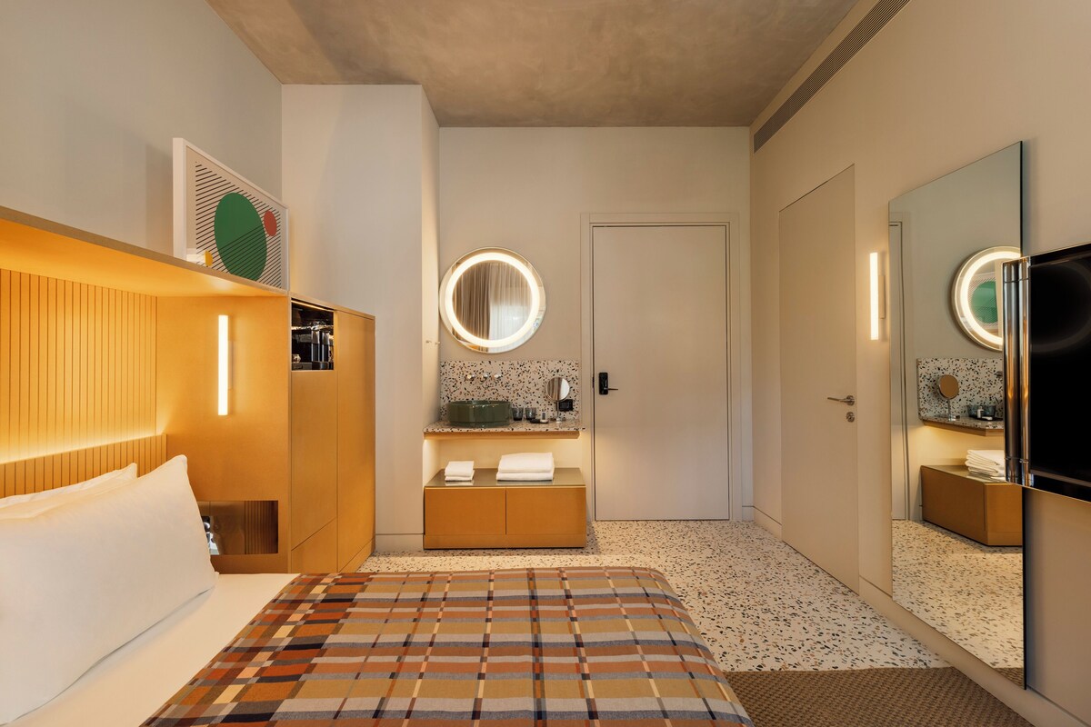 Una camera d'albergo con un letto, un comodino, uno specchio, un armadio e una televisione.