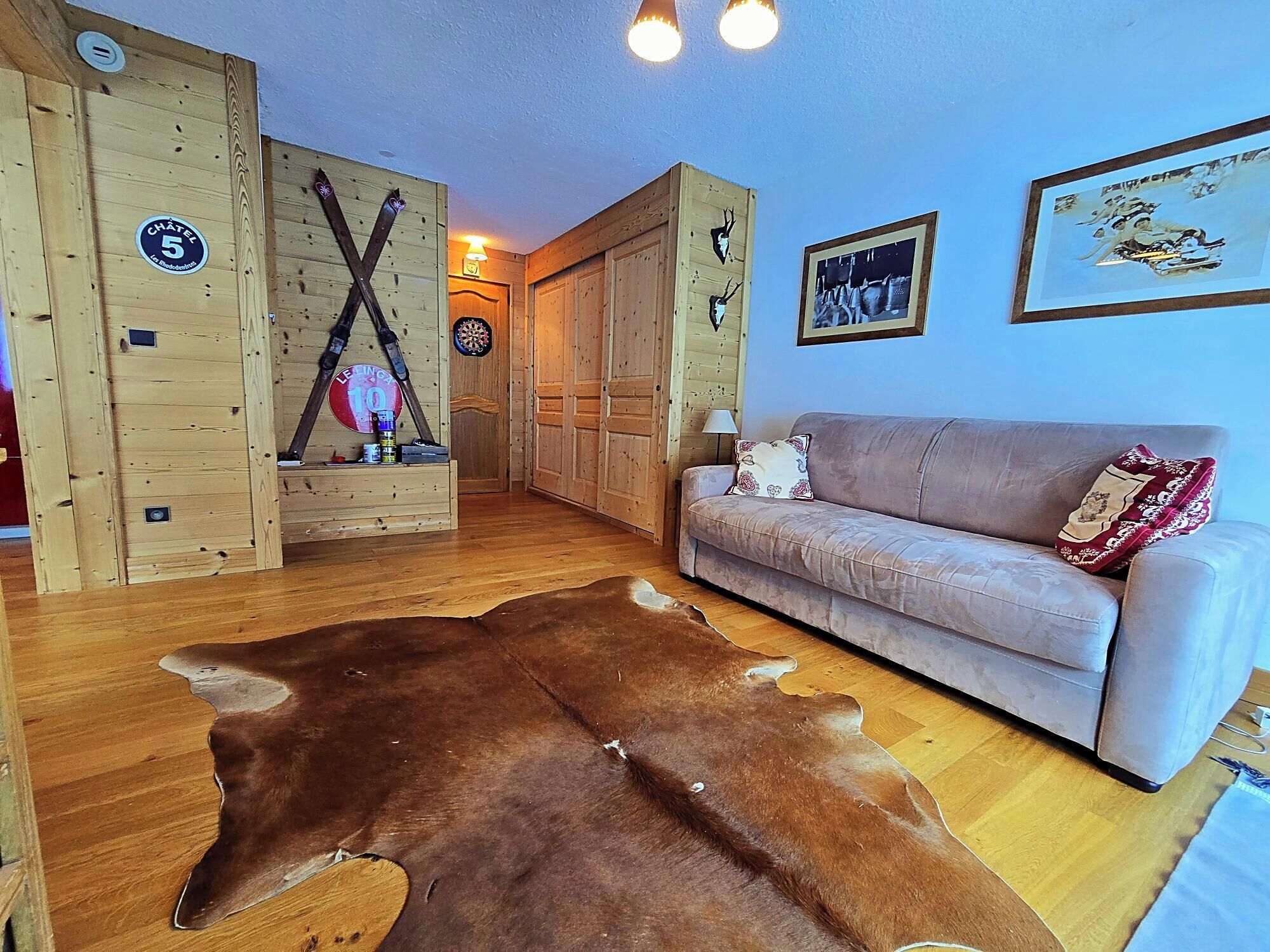 A room with wooden walls, a leather couch, a fur rug, and a dartboard.