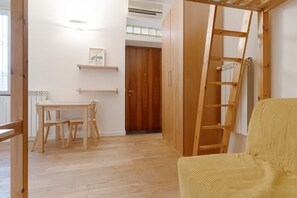 A room with a wooden floor, a wooden table with chairs, a wardrobe, a ladder, and a radiator.