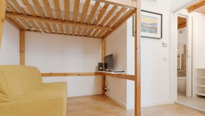 A room with a wooden ceiling structure, a yellow sofa, a television on a wooden stand, and a door leading to a bathroom. - GuestHost - Comfortable and practical 22 square meters studio apartment, perfect for two people, located on the second floor of a building without an elevator.The property is located in the Corvetto neighborhood, a lively area characterized by green spac (Milan)