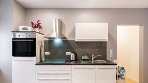 A modern kitchen with white cabinets, a stainless steel range hood, a built-in oven, and a sink. - Apartment “Zum Weißen Roß” with Shared Garden and Wi-Fi (Hausen)