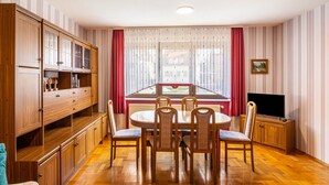 A dining area with a wooden table and chairs, a television, and a view through a window with curtains. - Apartment “Zum Weißen Roß” with Shared Garden and Wi-Fi (Hausen)