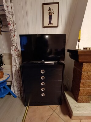 A room with a black entertainment unit, a framed picture on the wall, a blue stool, and a curtain with a floral pattern. - Nice 1-bedroom apartment in charming Cernesio perfect for relaxing stay (Cernesio)