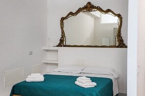 Un dormitorio con una cama, un espejo grande y una colcha color turquesa.