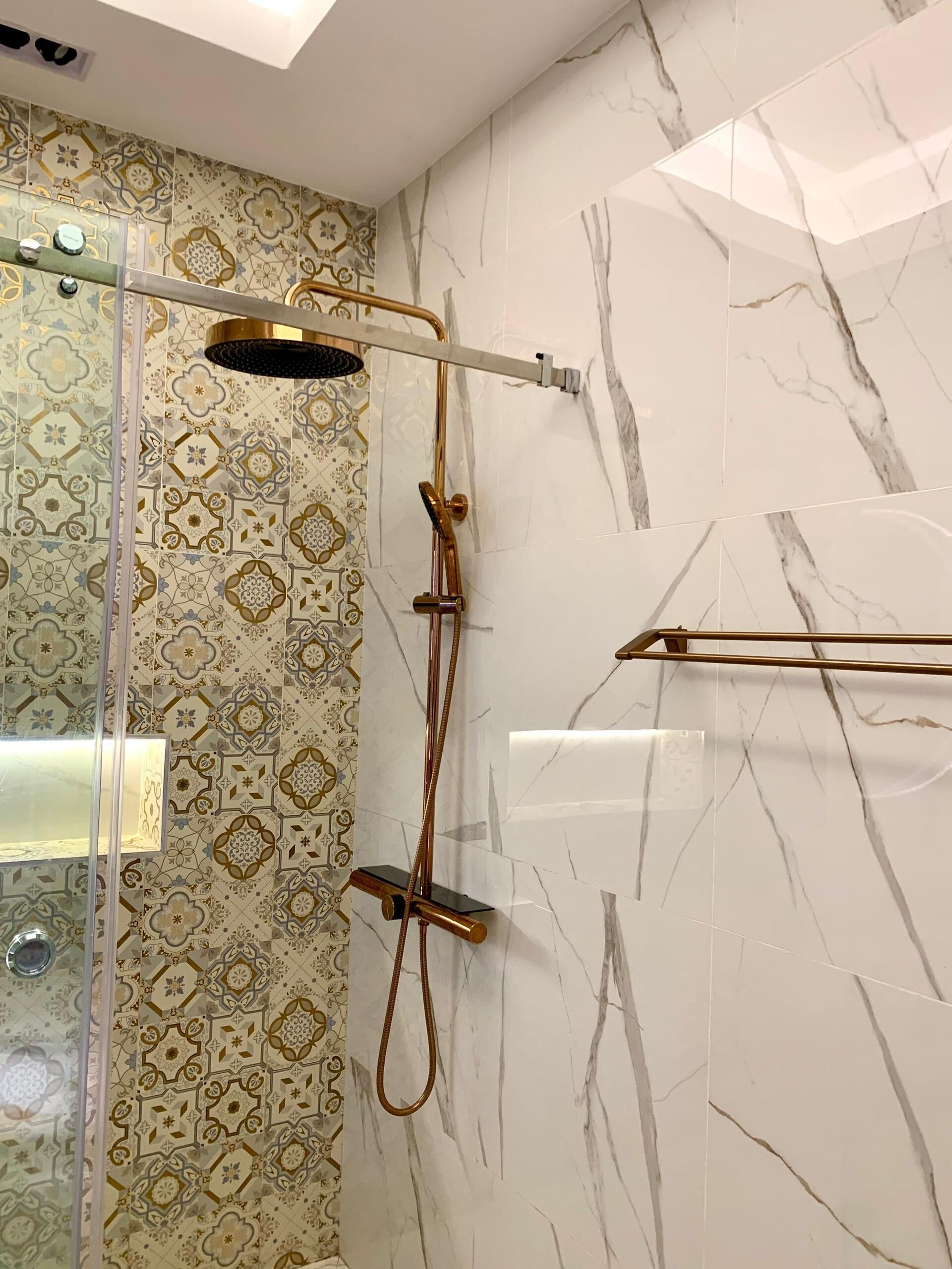 A bathroom with a shower area featuring a glass enclosure, a gold showerhead, and a patterned tile wall.