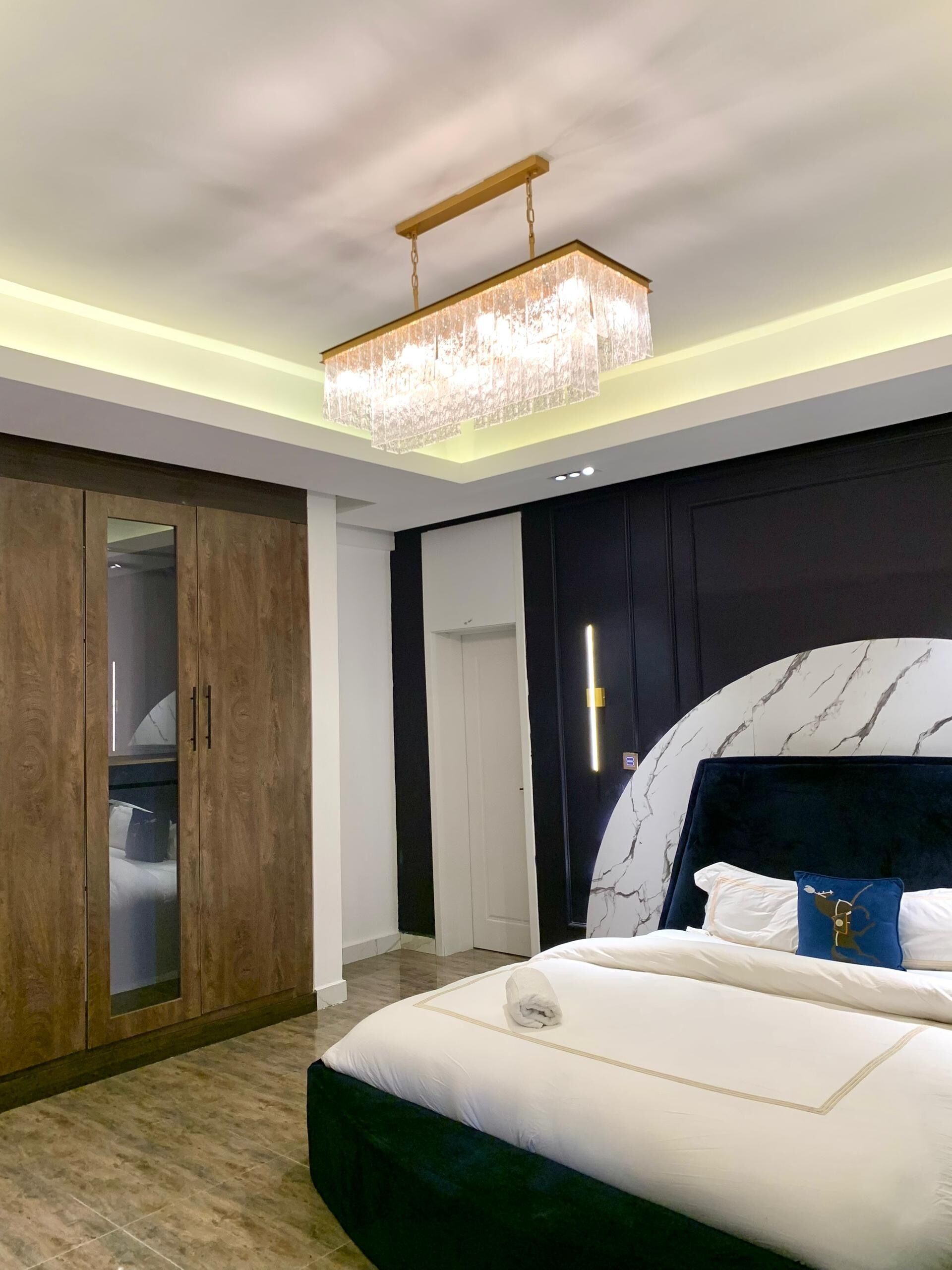 A modern bedroom with a large bed, a wooden wardrobe, and a chandelier.