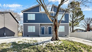 A two-story residential building with a symmetrical facade, a central entrance, and a tree in the front yard. - The Periwinkle Residence at Montgomery Row Residences (Clarksville)