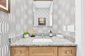 Ein Badezimmer mit einer Arbeitsplatte aus Granit, zwei Waschbecken, einem Spiegel und Wandpapier mit Muster.