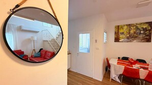 Ein Zimmer mit einem runden Spiegel an der Wand, einem Essbereich mit Tisch für zwei Personen und einer Treppe, die zu einer oberen Etage führt.