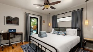 Habitación de hotel con cama, escritorio, silla, ventilador de techo y vistas al exterior.